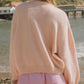 Woman in a cozy pink cardigan, enjoying a sunny day by the beach, wearing striped shorts.