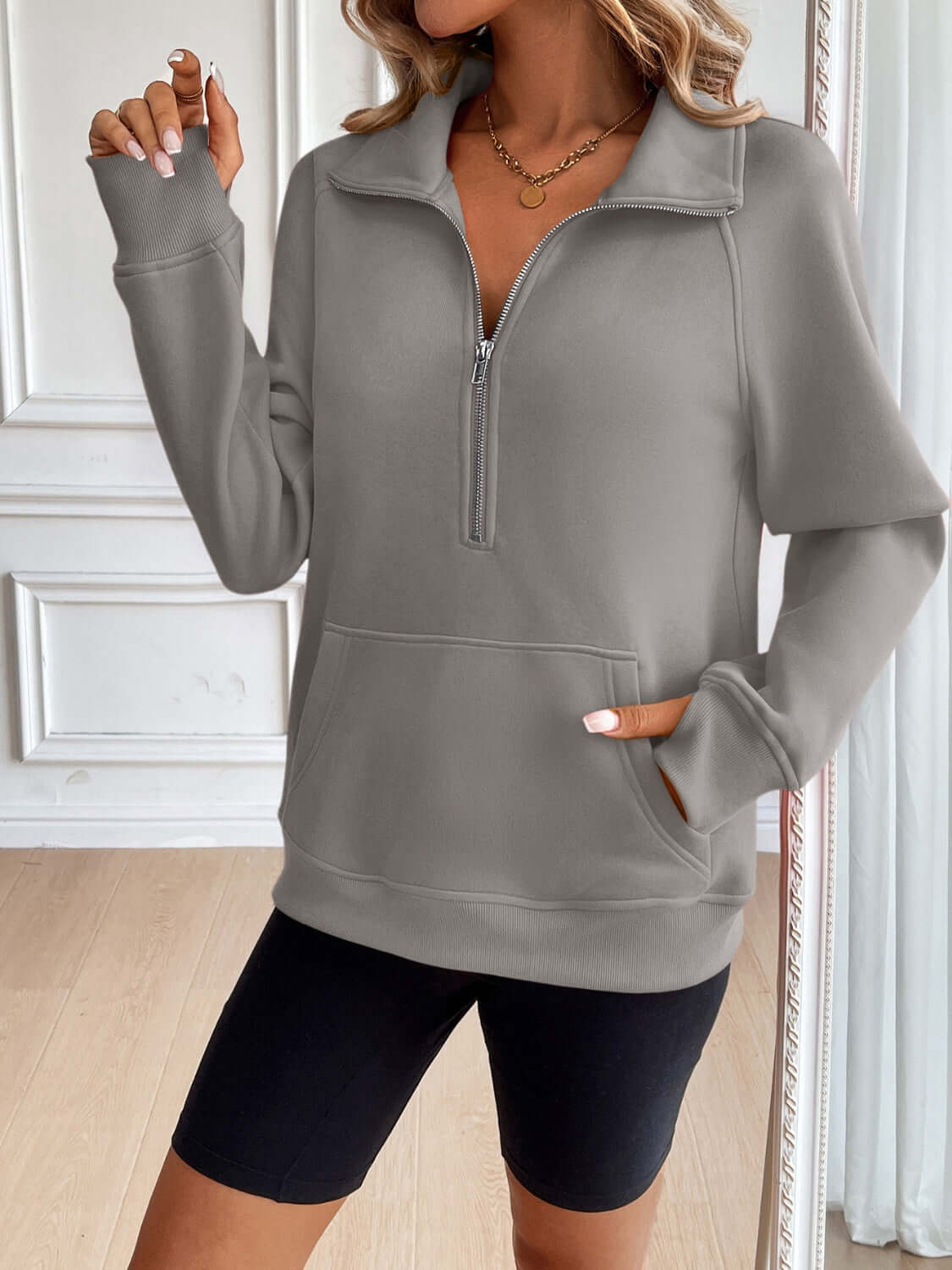 Woman wearing Ivy Lane Half Zip Raglan Sleeve Sweatshirt with pocket, shown in a room with light-colored walls.