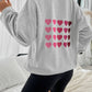 Woman wearing Devine Heart Dropped Shoulder Long Sleeve Sweatshirt with heart design on the back, paired with black shorts.