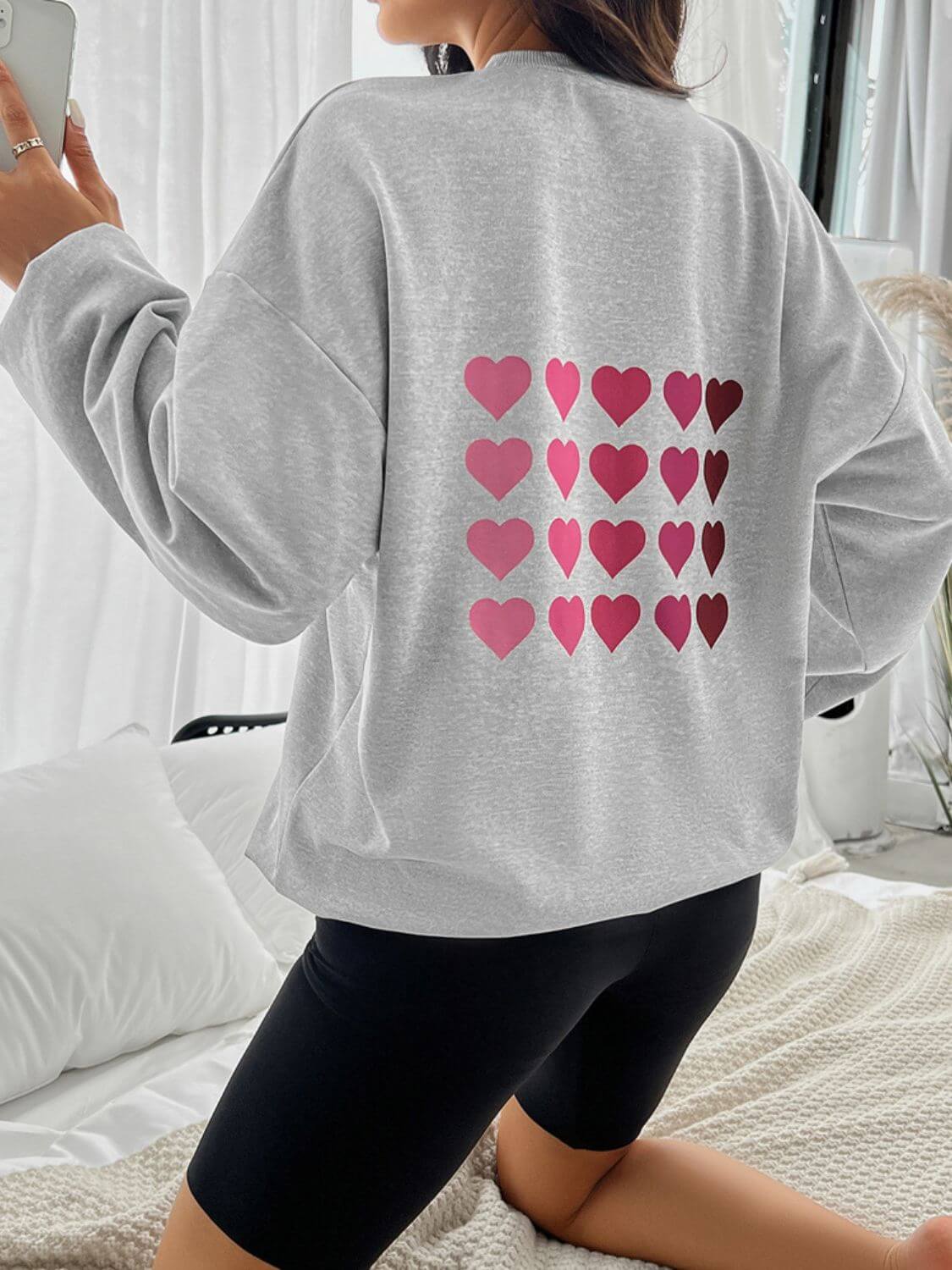 Woman wearing Devine Heart Dropped Shoulder Long Sleeve Sweatshirt with heart design on the back, paired with black shorts.