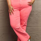 Woman wearing pink Risen Jeans with high waist and twill side detailing, standing against a wall, showcasing stylish and comfortable fit.