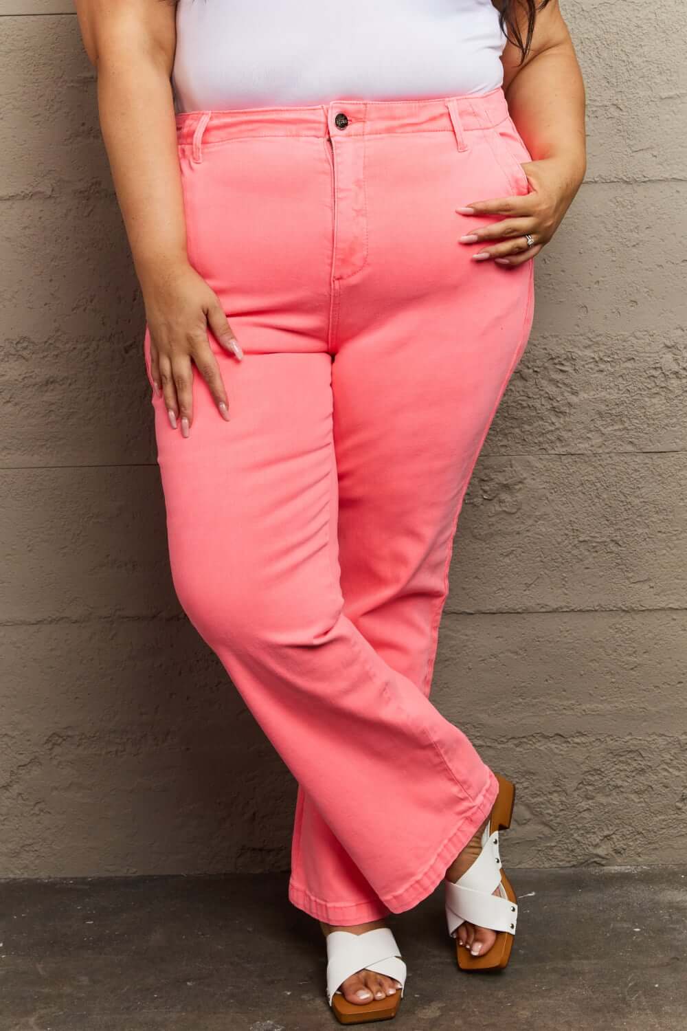 Woman wearing pink Risen Jeans with high waist and twill side detailing, standing against a wall, showcasing stylish and comfortable fit.