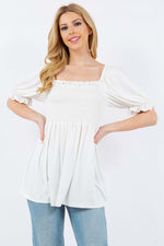 Woman wearing white ruffled short sleeve smocked blouse with delicate ruffles and smocked waist, paired with blue jeans