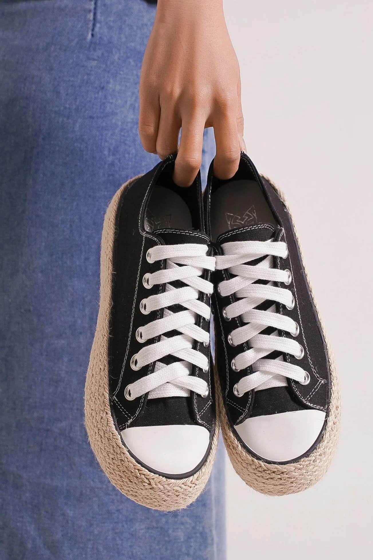 Black lace-up woven espadrille sole sneakers held by a person, perfect for summer style and comfort.