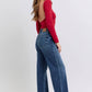 Model showcasing Judy Blue raw hem mid-rise jeans paired with a stylish red long-sleeve top, highlighting a trendy look.