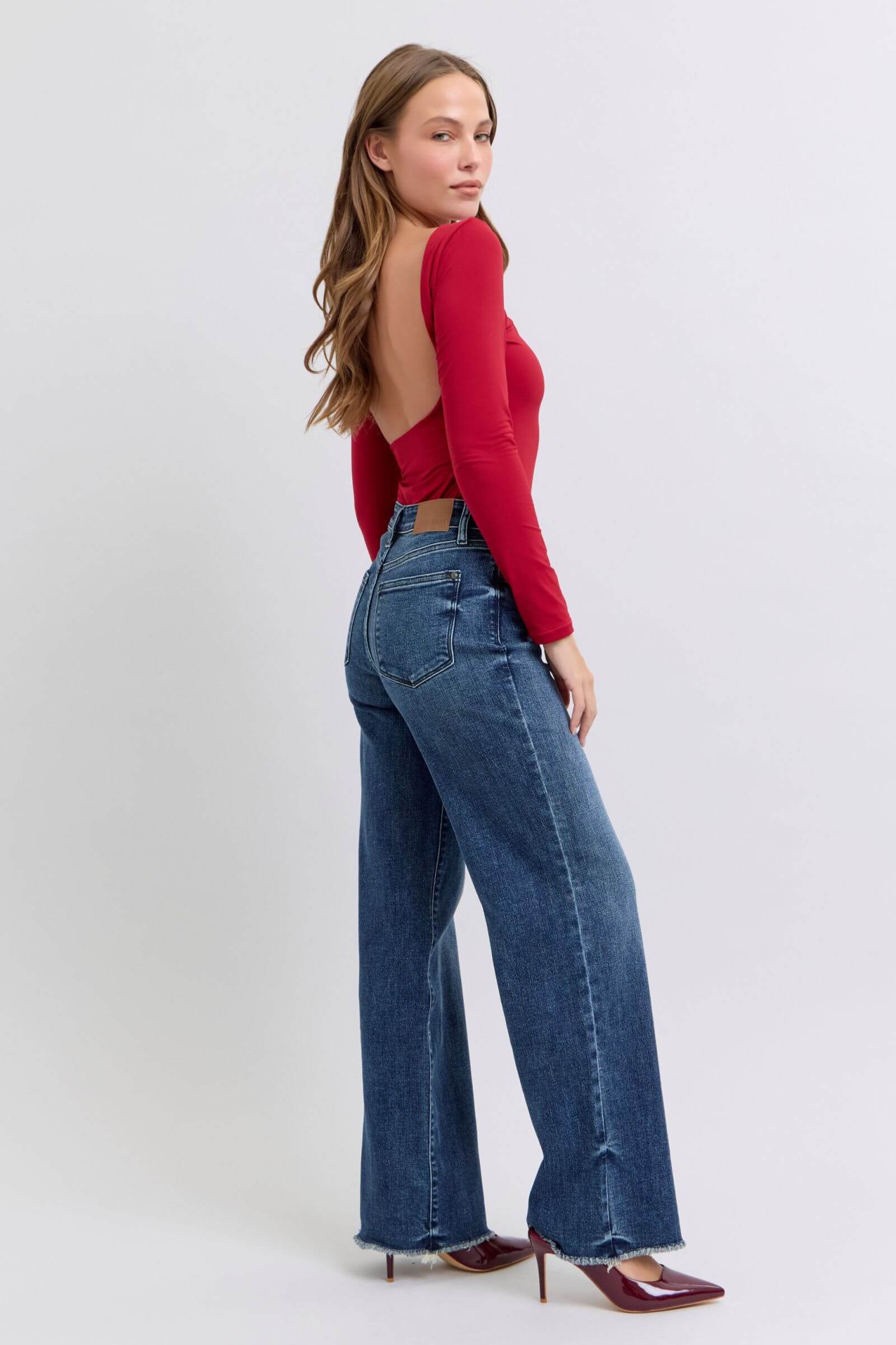 Model showcasing Judy Blue raw hem mid-rise jeans paired with a stylish red long-sleeve top, highlighting a trendy look.