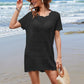 Stylish woman in a black openwork cover-up at the beach, enjoying summer vibes with a straw hat and bag.