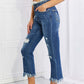 Woman wearing Risen Jeans undone chic straight leg jeans, featuring distressed details, raw hem, and cropped length, paired with casual sandals.