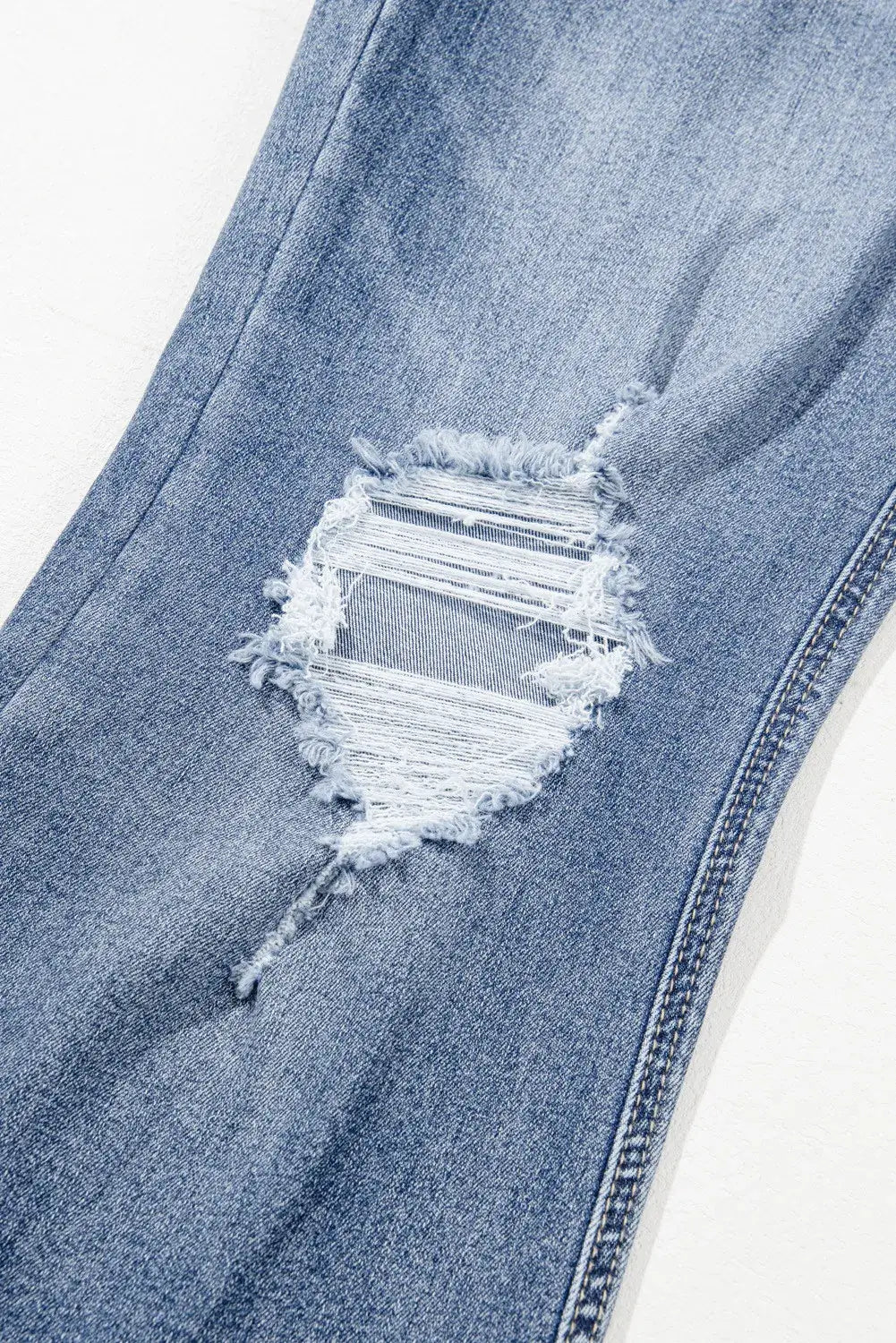 Close-up of distressed raw hem on slightly stretchy bootcut jeans made from cotton, polyester, and elastane blend.