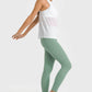 Woman in green ankle-length yoga leggings and white tank top, showcasing comfort and style for workouts.