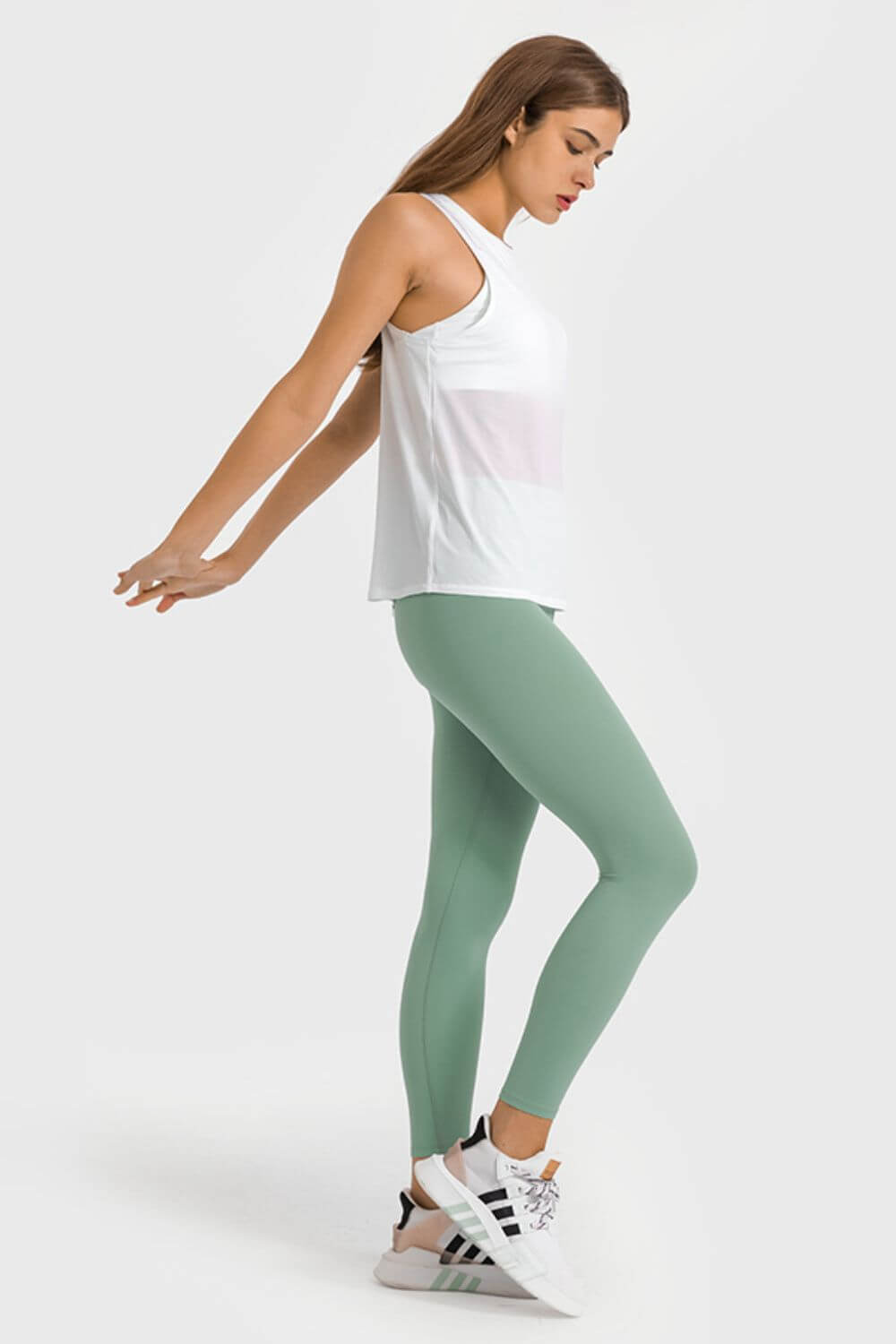 Woman in green ankle-length yoga leggings and white tank top, showcasing comfort and style for workouts.