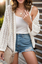 Woman wearing an openwork open front dropped shoulder cardigan over a white top and denim shorts, accessorized with a beige crossbody bag.