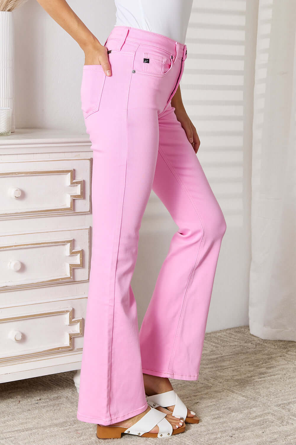 Pink high rise bootcut jeans with a flattering fit, elongating legs, and versatile style, paired with white sandals and a white top.