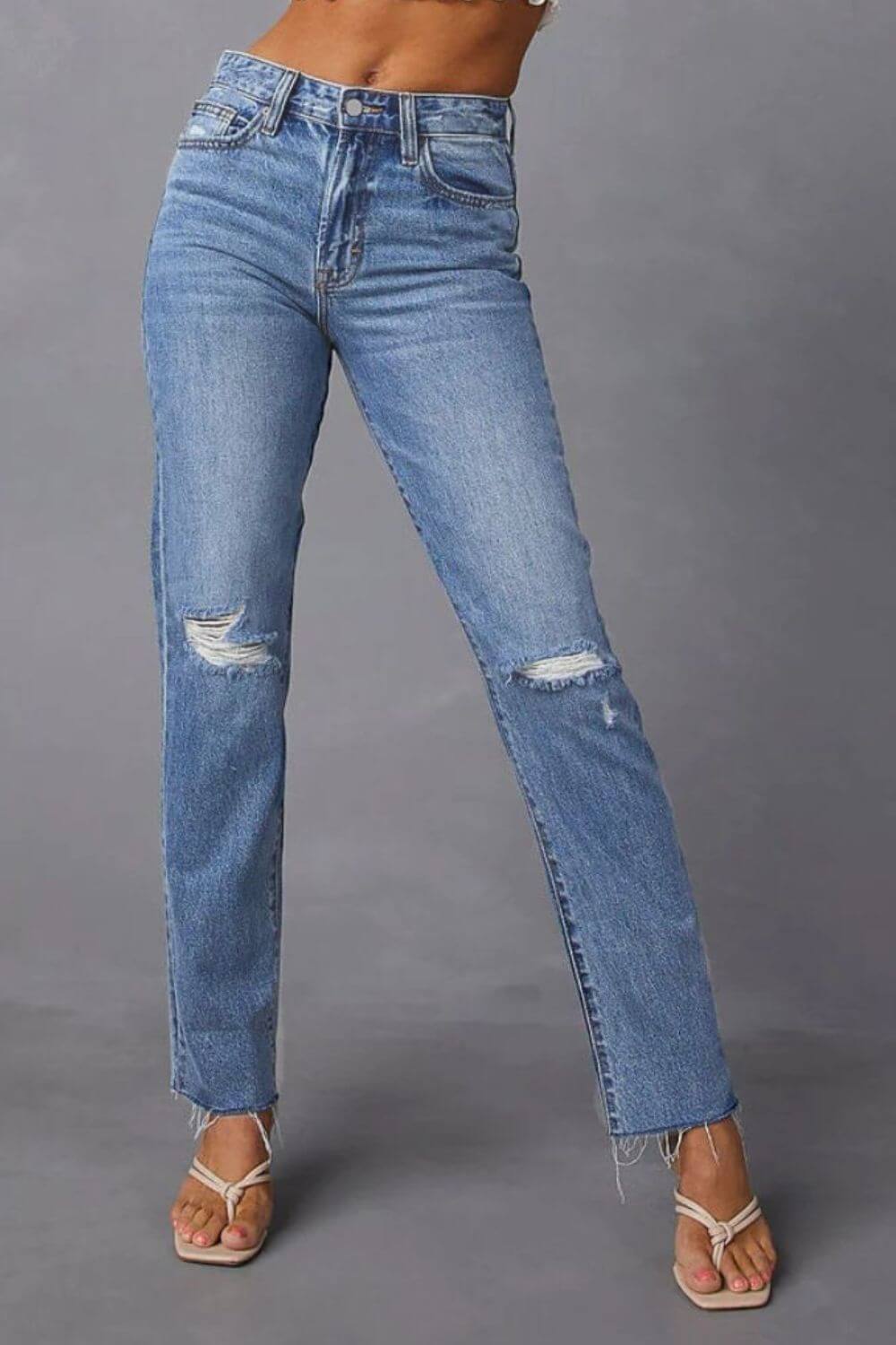 Distressed raw hem straight jeans with pockets, moderate stretch, trendy casual chic denim pants with ripped knees, front view.