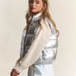 Shiny metallic puffer vest with snap and zipper closure, trendy winter fashion piece with sleek design and lightweight warmth.