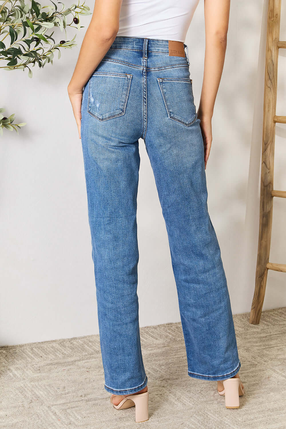 Back view of model wearing high waist distressed full-size Judy Blue Jeans with a white top and beige heels.