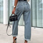 Woman wearing high waist wide leg jeans with black heels, holding black handbag and standing near large windows.