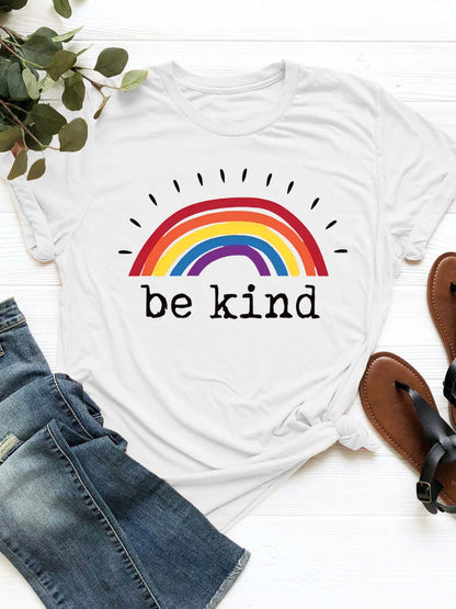 White graphic round neck short sleeve t-shirt with rainbow design and "be kind" text, styled with jeans and sandals.