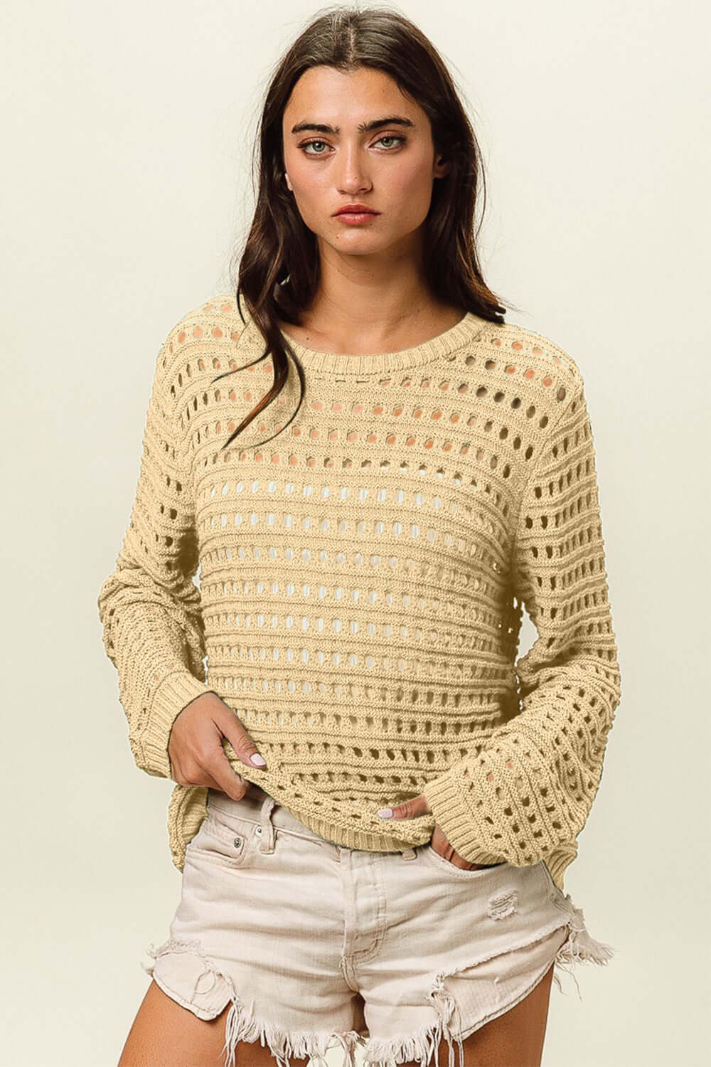 Woman wearing a round neck openwork knit cover up paired with white distressed shorts, showcasing a stylish and textured outfit layering piece.