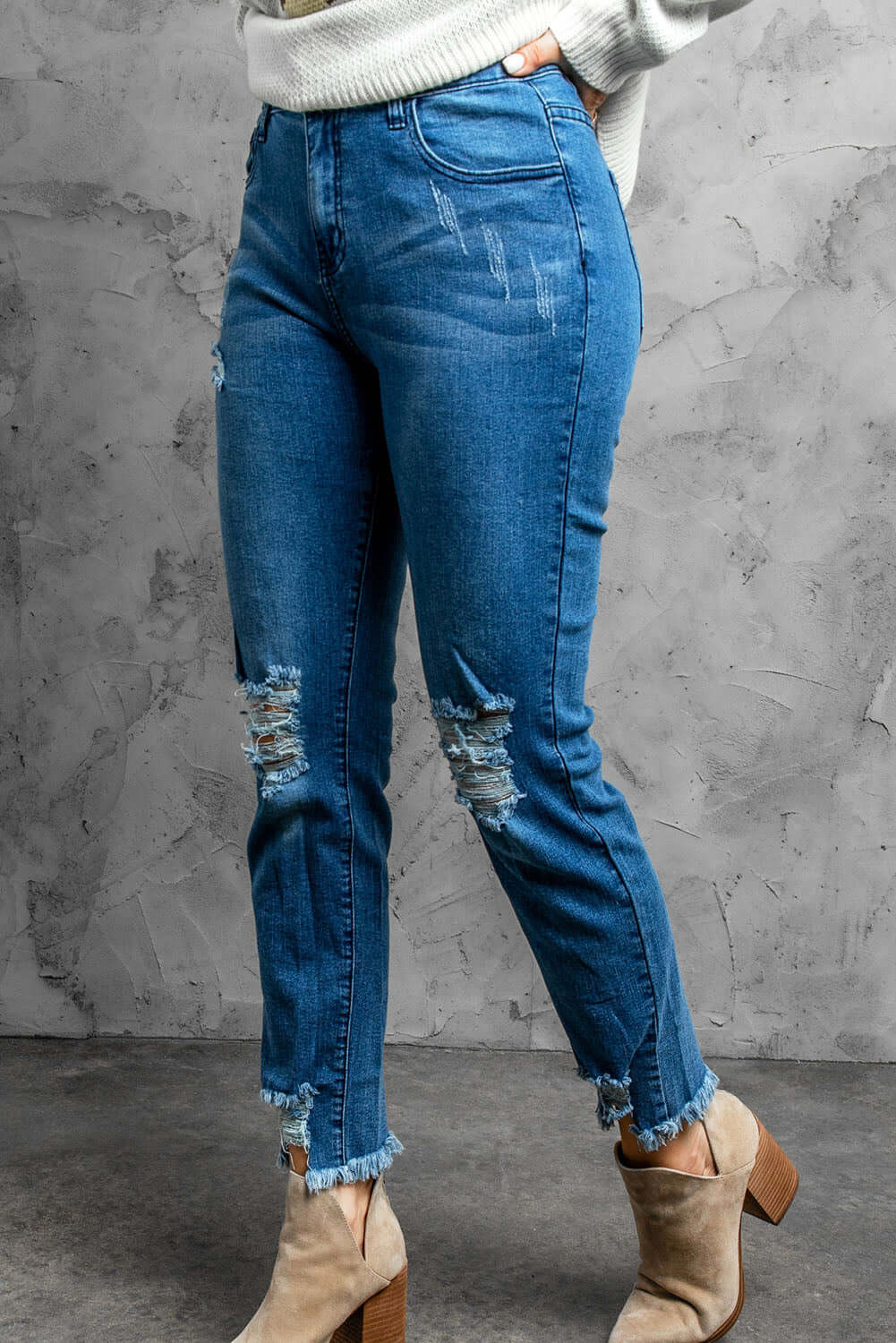 Stylish distressed cropped jeans with slightly stretchy material and raw hem, shown in a studio setting.