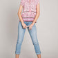 Woman wearing a pink print ruffle sleeve detail blouse paired with rolled-up light blue jeans and beige wedge sandals.