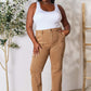 Model wearing Risen Jeans high waist straight jeans with pockets in beige, paired with a white tank top, standing near plants.