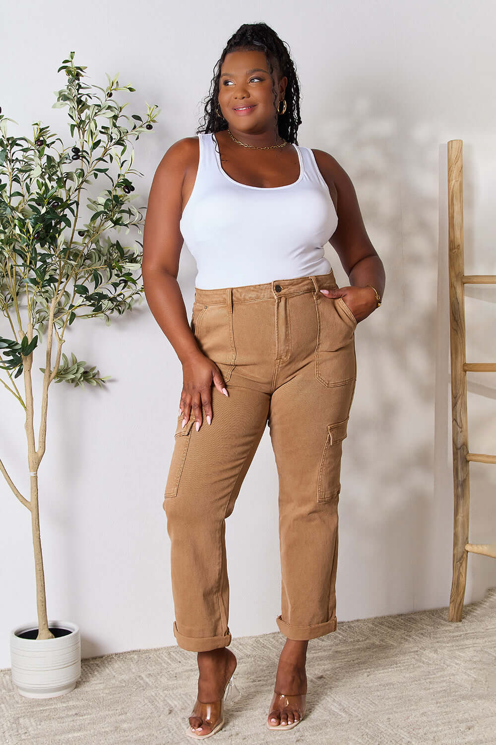 Model wearing Risen Jeans high waist straight jeans with pockets in beige, paired with a white tank top, standing near plants.