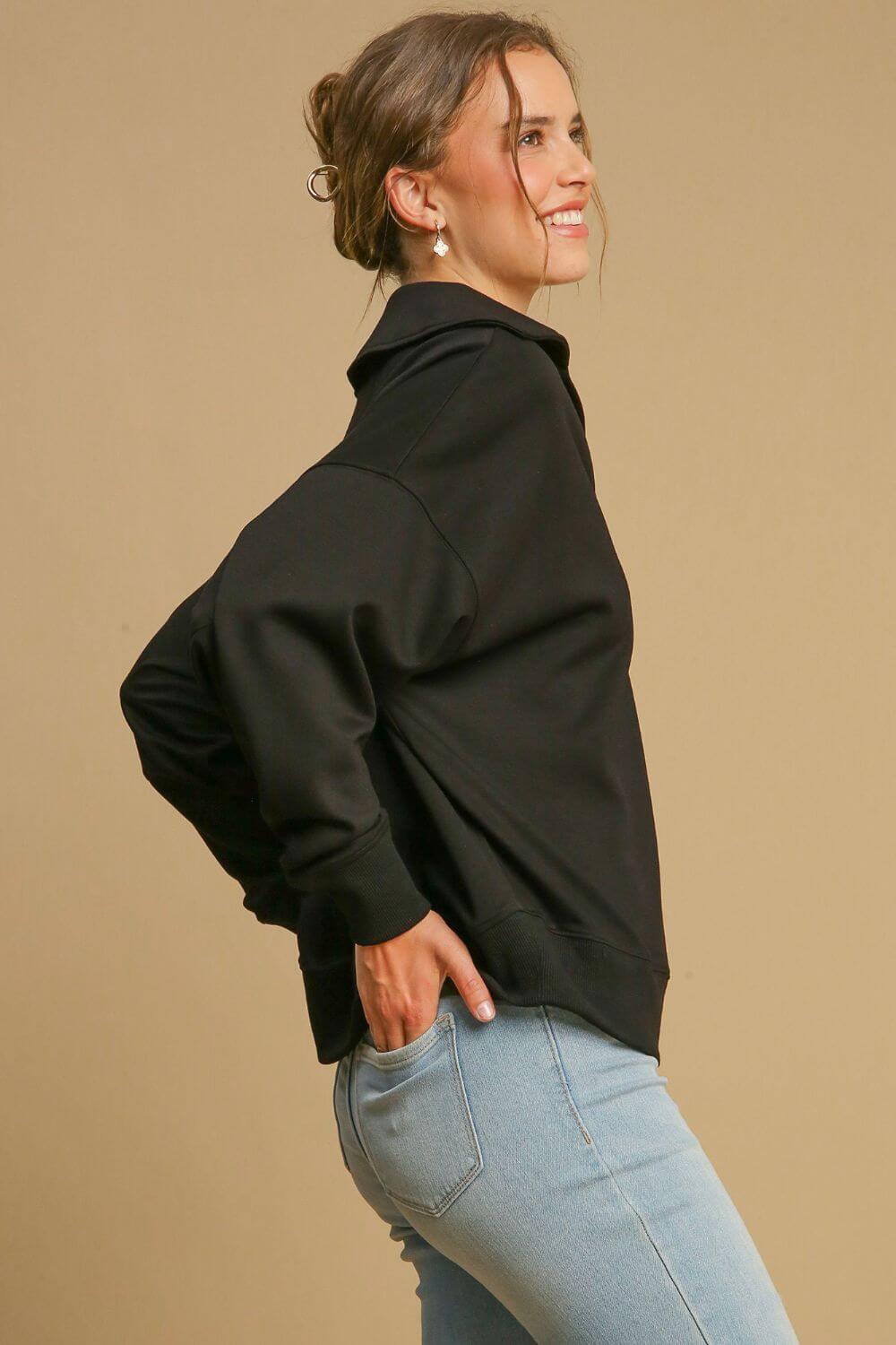 Woman wearing a black Johnny Collar Dropped Shoulder Sweatshirt, showcasing a relaxed fit and modern style with stylish jeans.