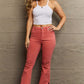 Woman modeling Bailey High Waist Side Slit Flare Jeans by Risen Jeans in coral, paired with a white crop top and platform sandals.