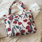 Medium printed canvas handbag with red floral design and zipper lying on a white fabric background.