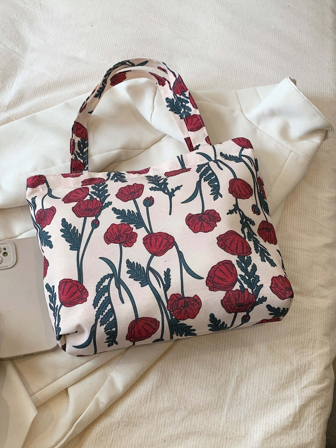 Medium printed canvas handbag with red floral design and zipper lying on a white fabric background.