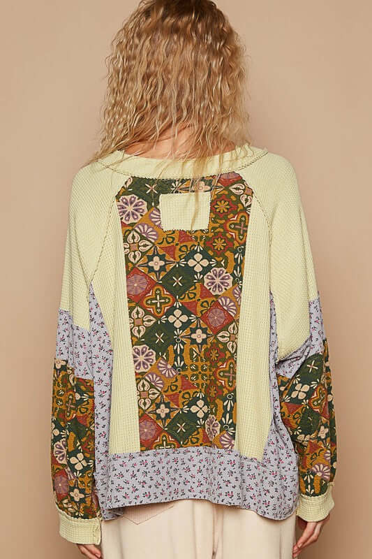 Back view of a trendy raglan sleeve top featuring a unique patchwork design and exposed seams in earthy tones.