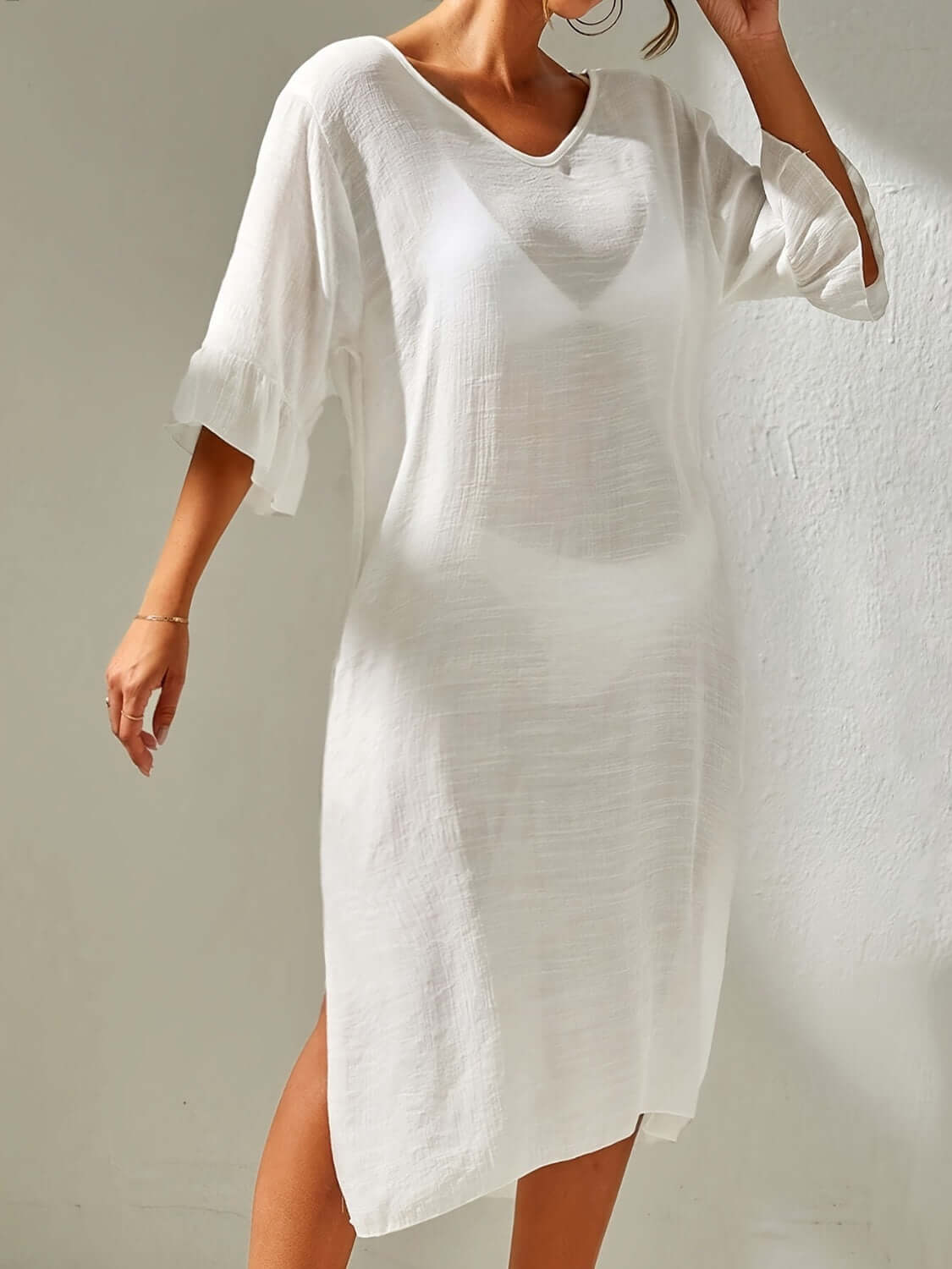 Woman wearing a white slit V-neck flounce sleeve cover-up dress made of sheer polyester.