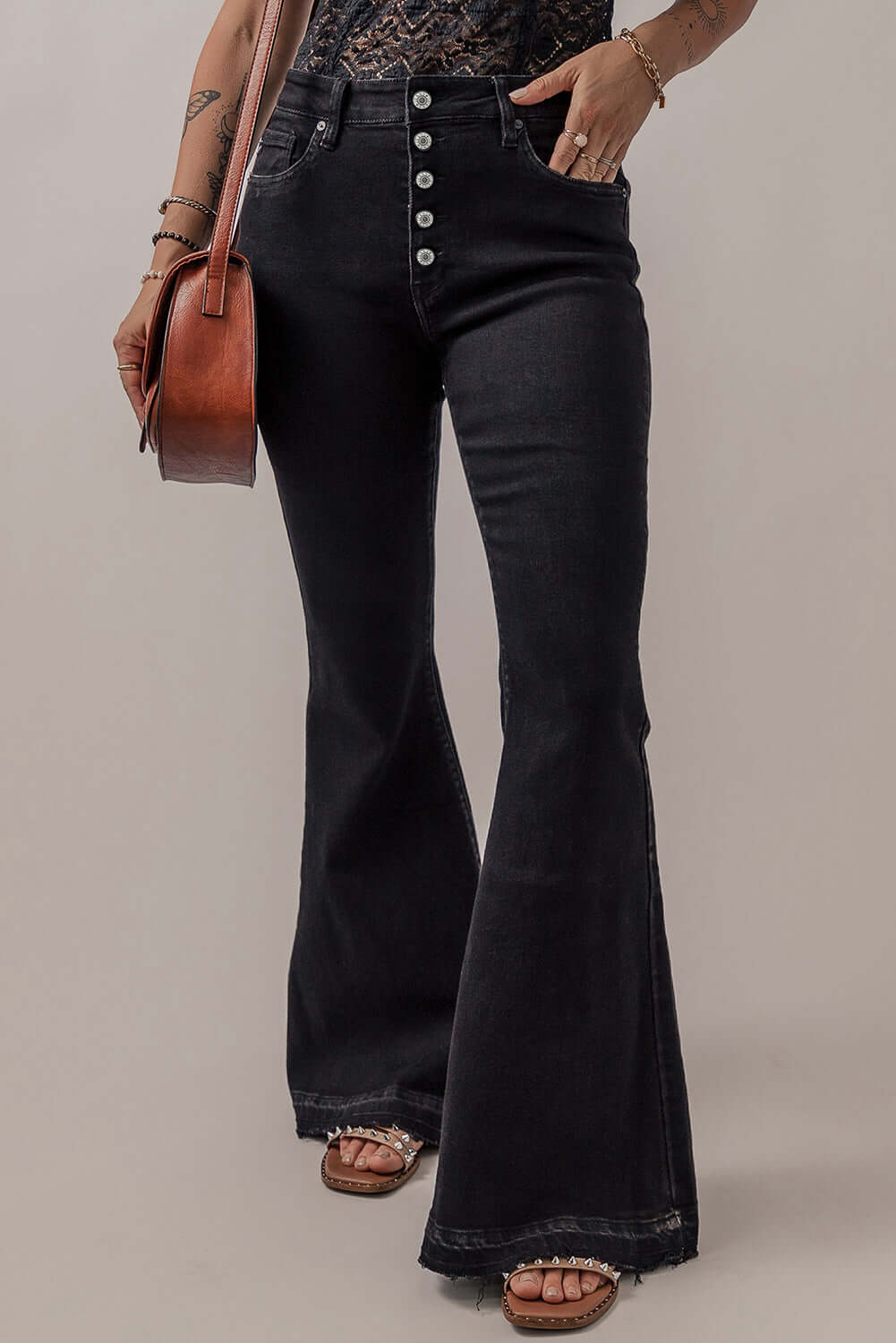 Woman wearing Bella Road Button-Fly Flare Jeans with pockets, showcasing stylish black denim fabric and button details, paired with a brown bag.