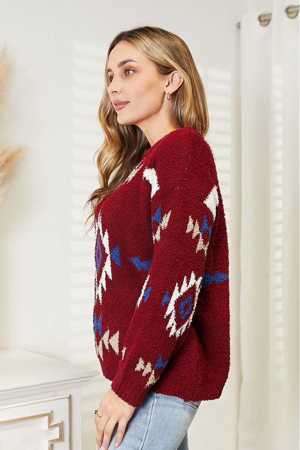 Woman wearing HEYSON Full Size Aztec Soft Fuzzy Sweater in red, featuring a vibrant Aztec pattern, standing in a bright room.