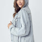 Young woman wearing a distressed denim jacket with a drawstring hood, showcasing a casual and stylish look.