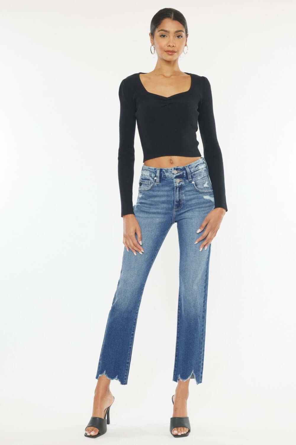 Woman wearing Kancan High Rise Slim Straight Jeans in medium stone wash with frayed hem and stylish black top, showcasing trendy fashion.