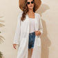 Woman wearing a lace detail open front long sleeve cover-up, white tank top, denim shorts, sunhat, and sunglasses