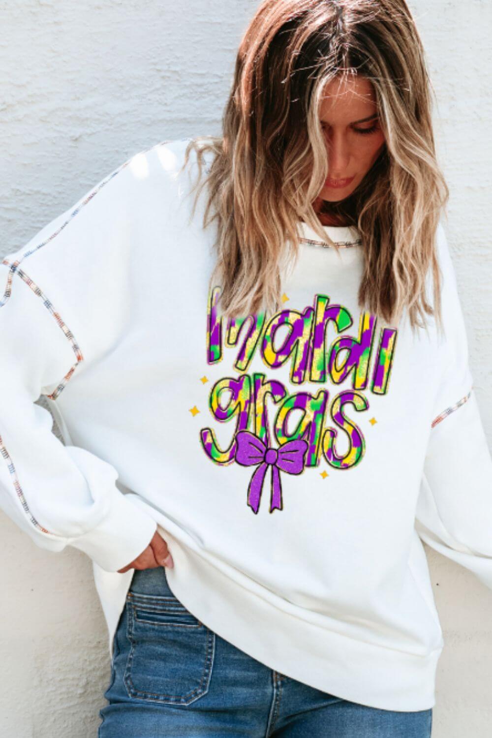 Woman wearing Bella Road Mardi Gras sweatshirt with colorful lettering and bow detail, perfect for festive celebrations.