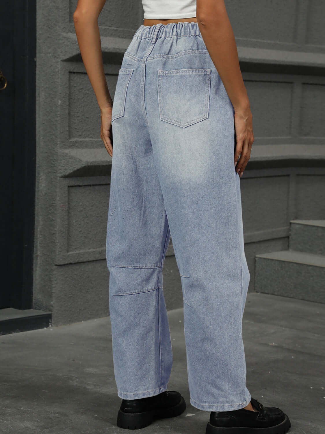 Woman wearing light wash half elastic waist straight leg jeans with back pockets.