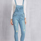 Woman wearing distressed washed denim overalls with pockets, slightly stretchy mid waist fit, made of 65% cotton and 35% polyester