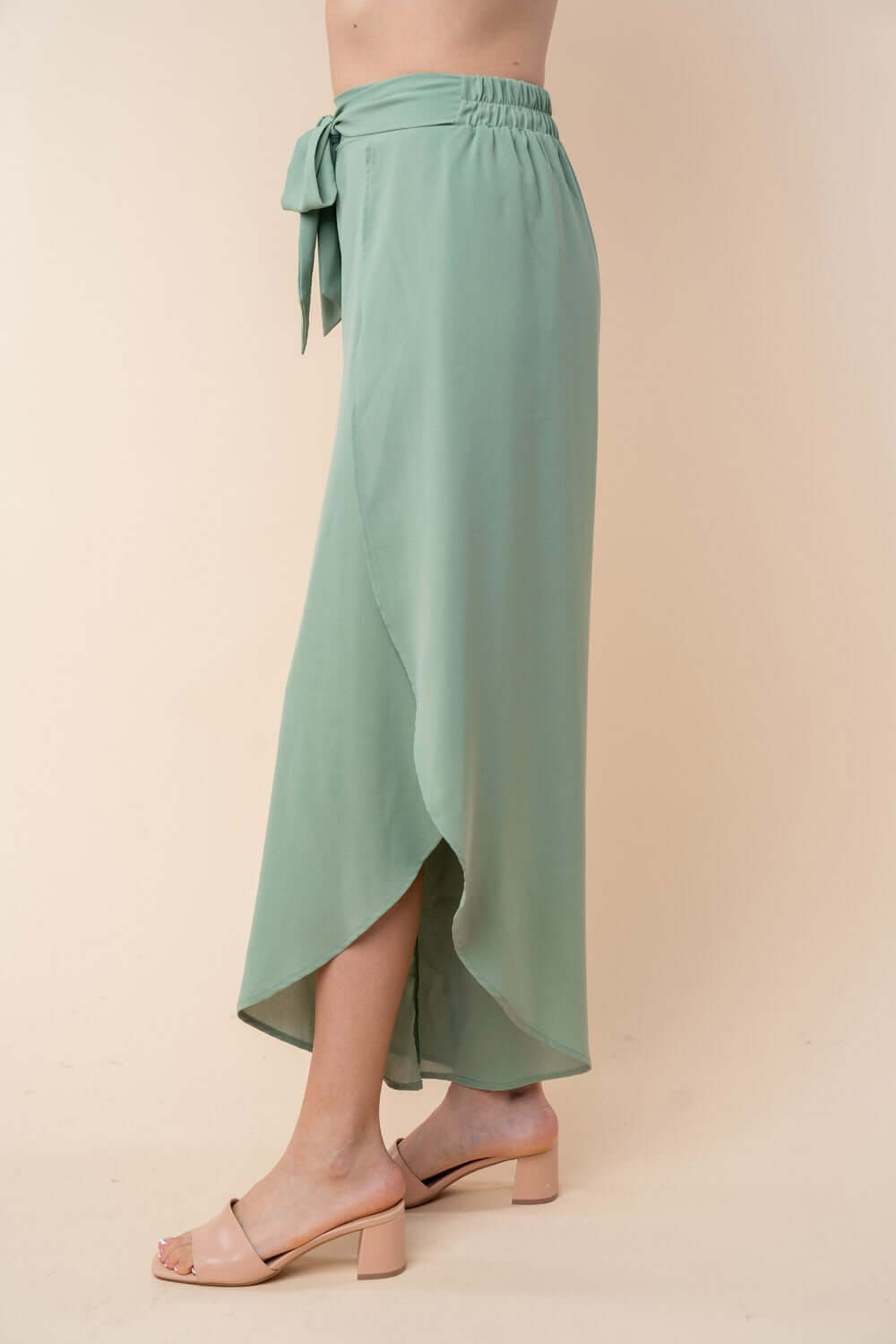 High-waisted woven pants with wide tulip hem in green, featuring an elastic waist and built-in shorts, modeled with beige block heels