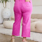 Woman wearing Crop Chloe Full Size Tummy Control High Waist Raw Hem Jeans in pink, styled with a white top and wedge sandals.