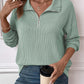 Woman wearing a striped half zip long sleeve t-shirt in light green, holding a coffee cup.