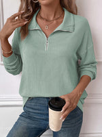 Woman wearing a striped half zip long sleeve t-shirt in light green, holding a coffee cup.