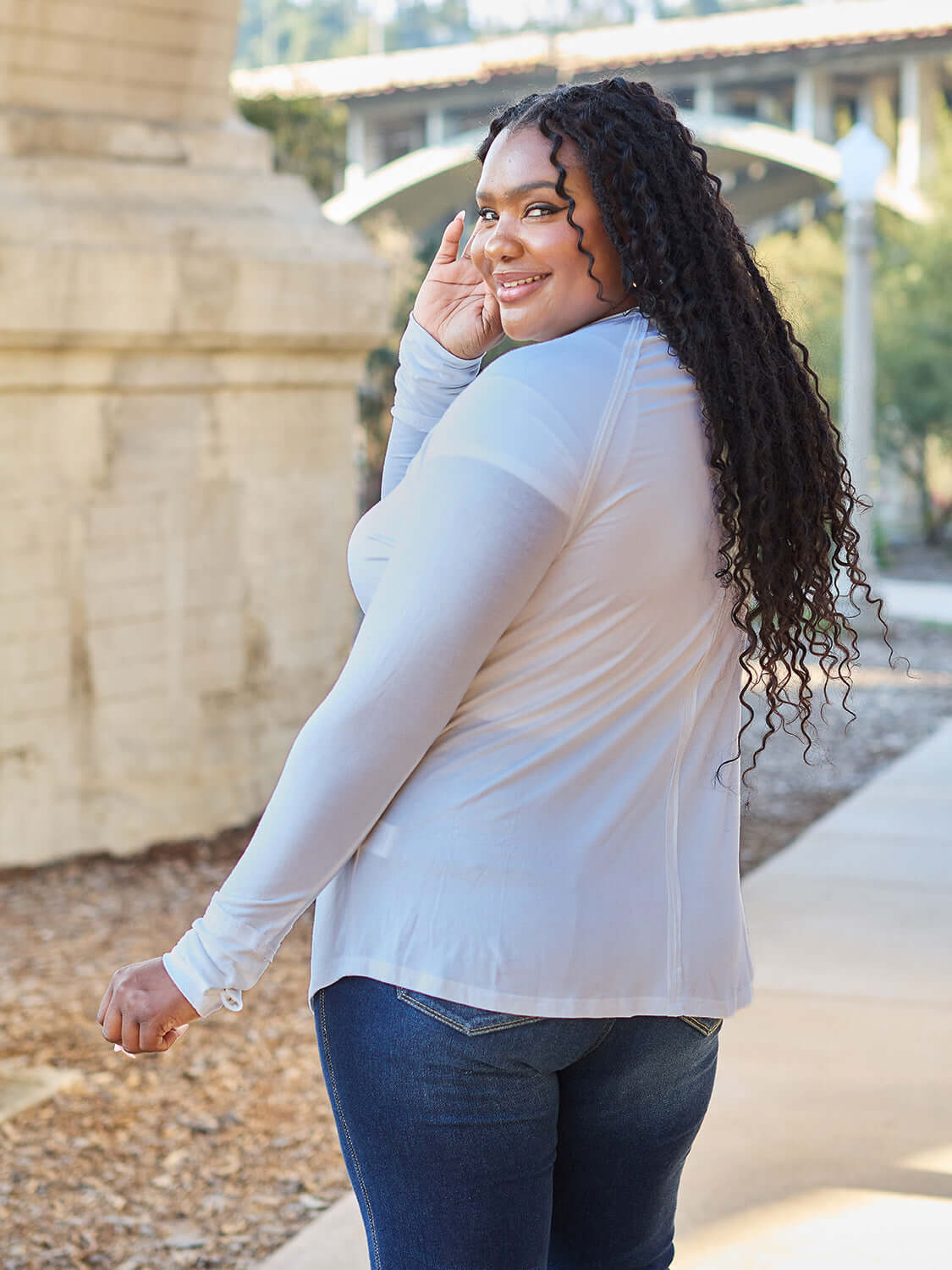 Smiling model wearing a round neck long sleeve t-shirt in white, paired with blue jeans, standing outdoors.