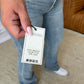 Woman holding tag on Judy Blue medium rise bootcut jeans, showcasing classic blue denim style and comfortable fit.