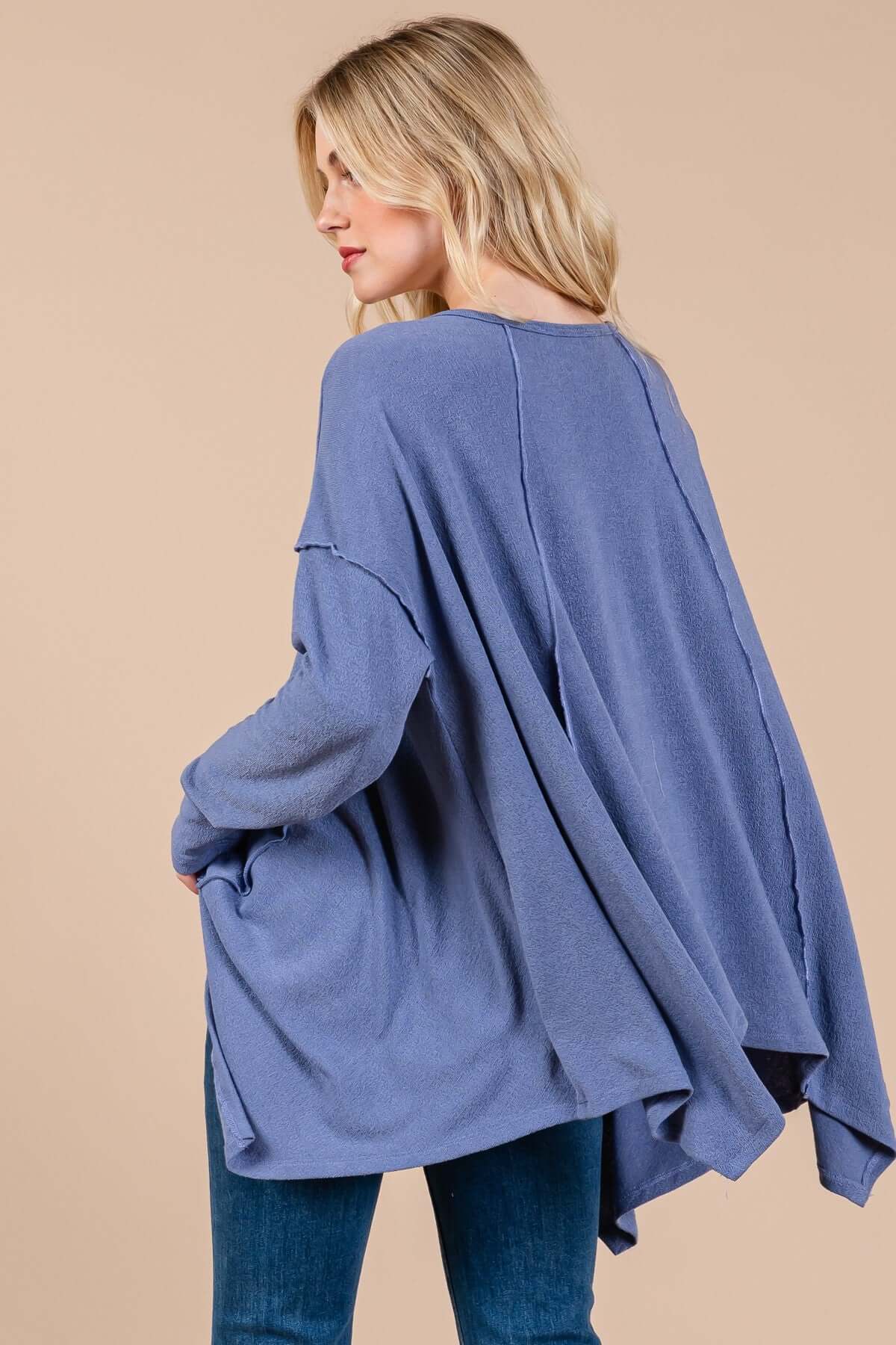 Woman wearing Ces Femme asymmetrical long sleeve top in blue, showcasing a relaxed fit with a hi-low hem and drop sleeves.