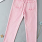 Pink raw hem button-fly jeans with back pockets for petites laid flat on a grey background.