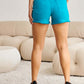 Back view of woman wearing Tummy Control High Waist Raw Hem Denim Shorts by RFM Jeans in teal color.